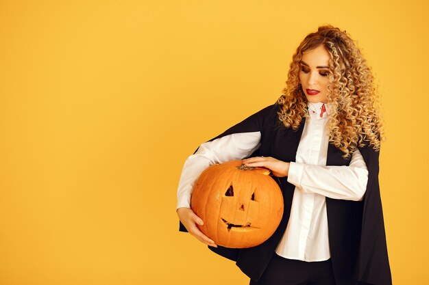 Frau, die schwarzes Kostüm trägt. Dame mit Halloween Make-up. Mädchen, das auf einem gelben Hintergrund steht.