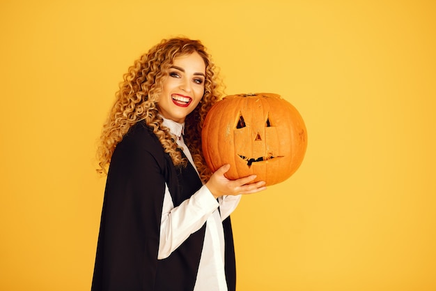 Frau, die schwarzes Kostüm trägt. Dame mit Halloween Make-up. Mädchen, das auf einem gelben Hintergrund steht.