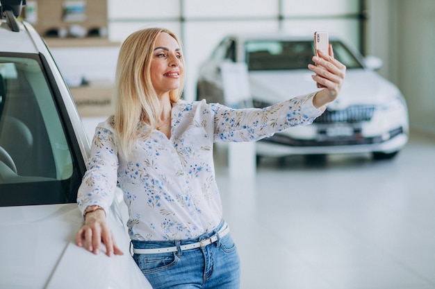 Frau, die selfie durch das Auto in einem Autoausstellungsraum tut