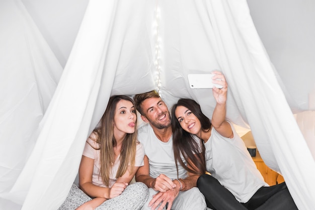Frau, die selfie mit ihren Freunden sitzen auf Bett nimmt