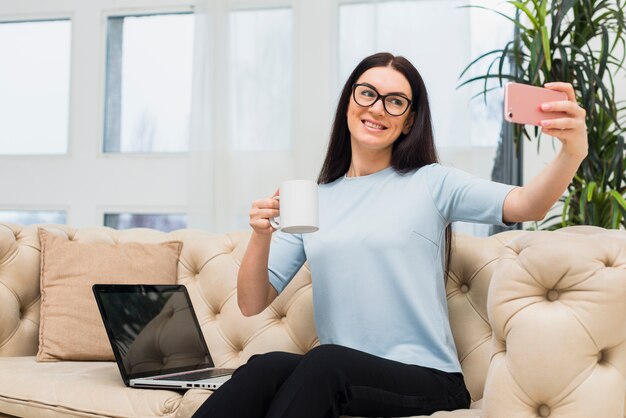 Frau, die selfie mit Kaffee auf Couch nimmt