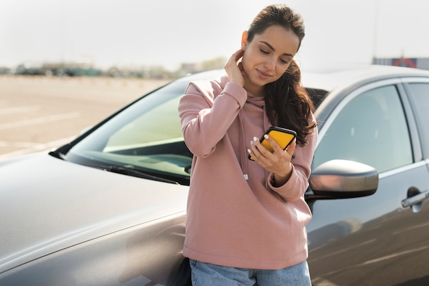 Frau, die sich auf das Auto stützt und auf ihr Telefon schaut