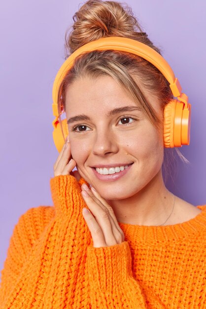 Frau, die sich auf die Ferne konzentriert, hat einen fröhlichen Ausdruck, der über Stereo-Kopfhörer in einem Strickpullover gekleidet ist und Lieblingsmusik isoliert auf Lila genießt