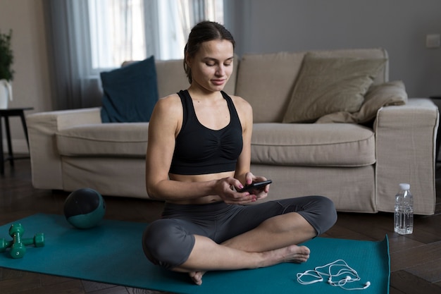 Frau, die sich auf Yogamatte hinsetzt und Smartphone verwendet