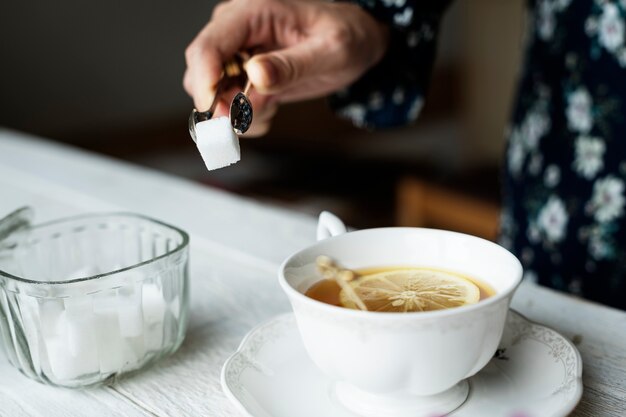 Frau, die sich mit einem Zuckerwürfel für ihre Schale des netten heißen Zitronentees hilft