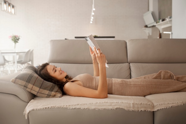 Frau, die sich zu Hause digital trennt, indem sie ein Buch auf der Couch liest
