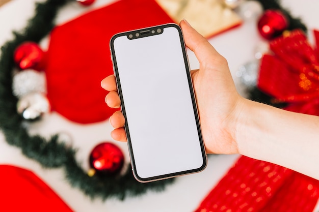 Frau, die Smartphone nahe Weihnachtsbaumdekoration hält