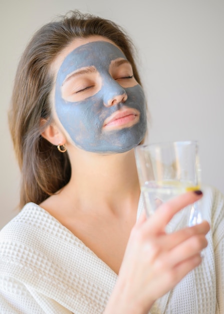 Frau, die Spa zu Hause mit Gesichtsmaske und Wasser genießt