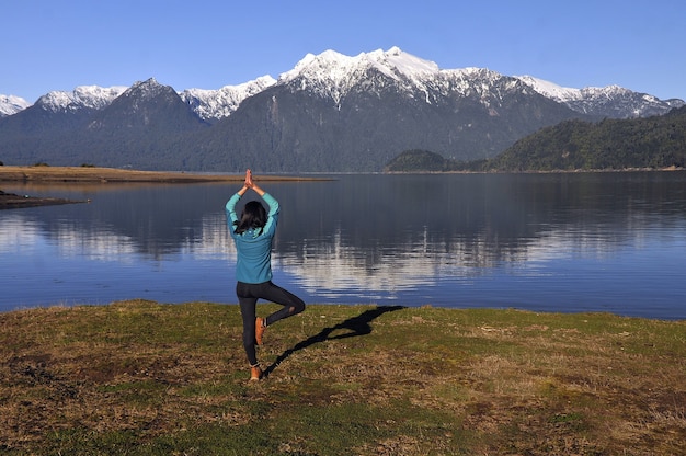 Frau, die Sportbekleidung trägt und eine Yoga-Pose vor dem ruhigen See und den Bergen hält