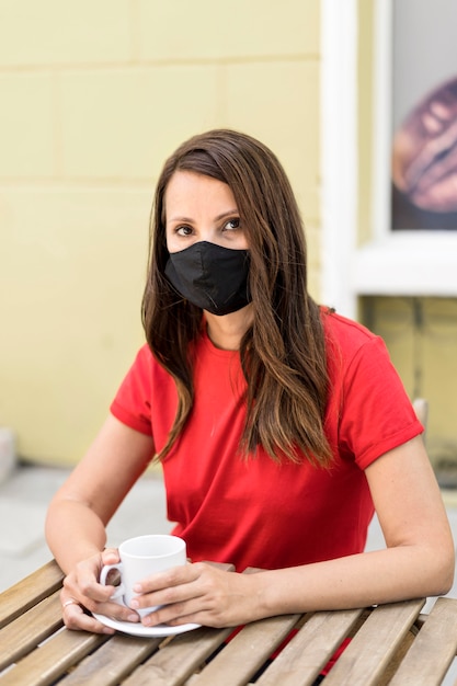 Frau, die Stoffmaske trägt und eine Tasse Kaffeeansicht hält