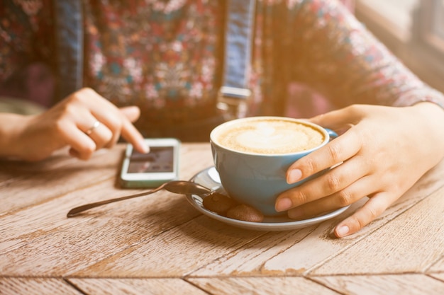 Frau, die Tasse Kaffee bei der Anwendung des Mobiltelefons hält