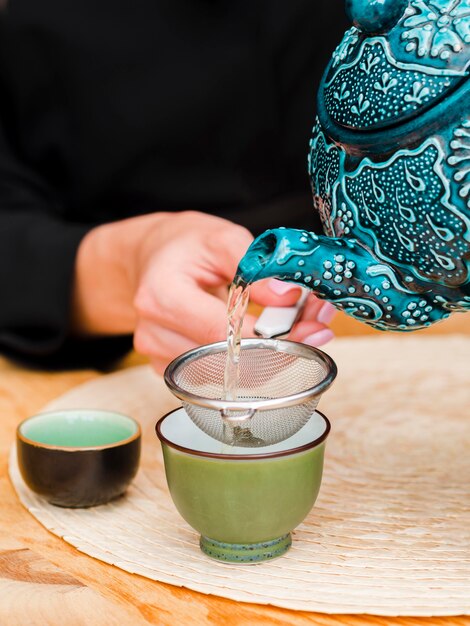 Frau, die Tee in Teetasse mit Sieb gießt