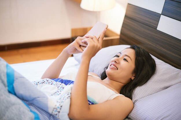 Frau, die Telefon beim Lügen im Bett verwendet