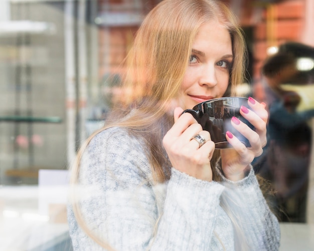 Kostenloses Foto frau, die von der schale am fenster trinkt