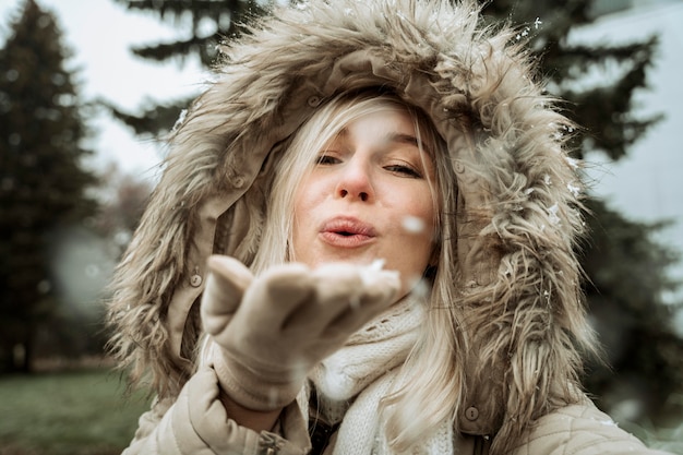 Frau, die von ihrer Hand in den Schnee bläst