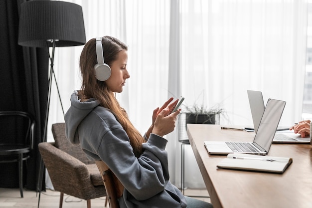 Frau, die von zu Hause aus am Schreibtisch mit Kopfhörern und Smartphone arbeitet