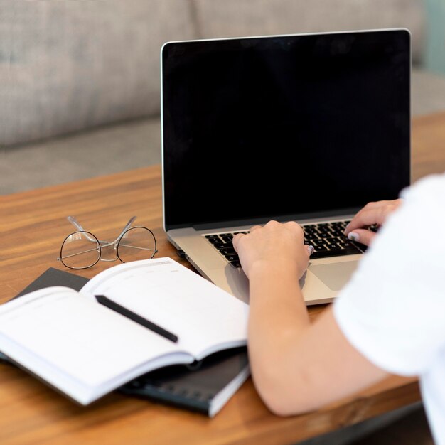 Frau, die von zu Hause aus für soziale Distanzierung mit Laptop und Notizbuch arbeitet