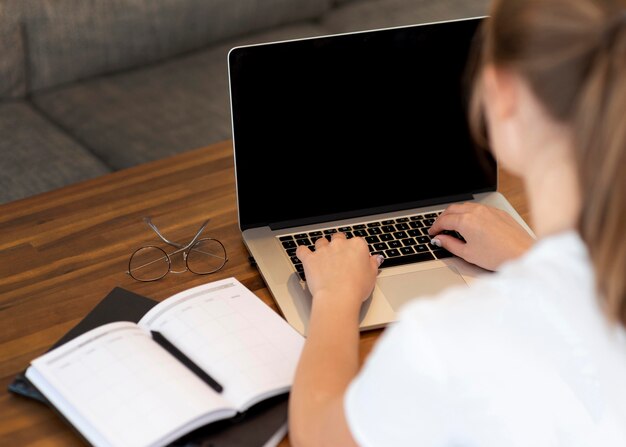 Frau, die von zu Hause aus für soziale Distanzierung mit Notizbuch und Laptop arbeitet