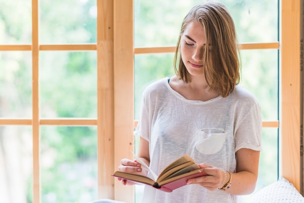 Kostenloses Foto frau, die vor fensterlesebuch steht