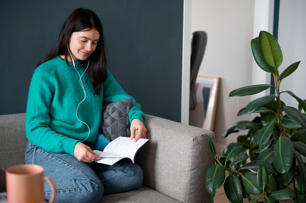 Frau, die während der Quarantäne zu Hause Musik hört und ein Buch liest