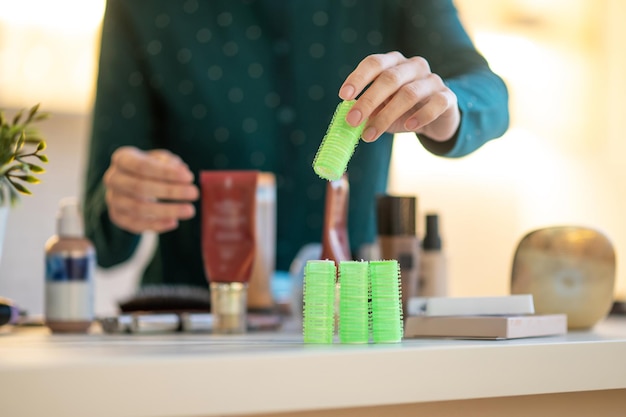 Frau, die während des Online-Tutorials zum Haarstyling grüne Lockenwickler in den Händen hält