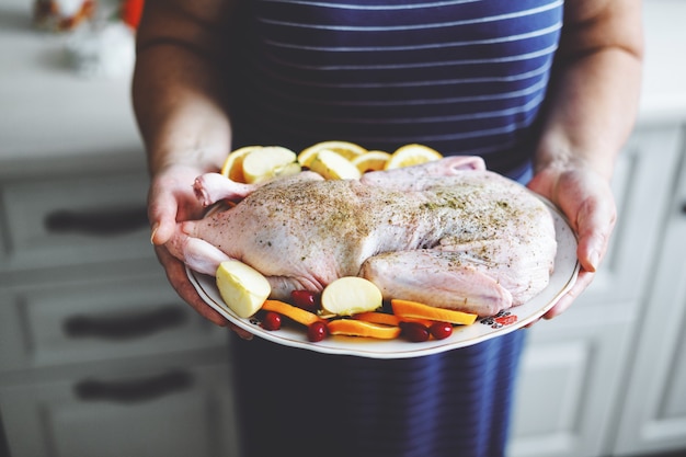 Frau, die Weihnachtsente kocht, die rohe Ente mit Gemüse im Ofen setzt.