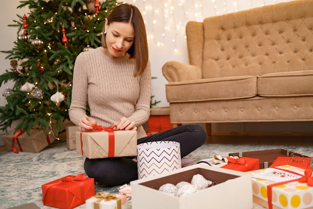 Frau, die weihnachtsgeschenk verpackt, während sie auf dem teppich im wohnzimmer sitzt