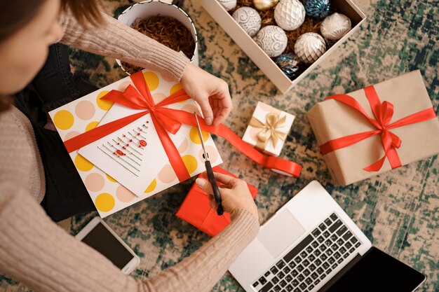 Frau, die Weihnachtsgeschenk verpackt, während sie auf dem Teppich im Wohnzimmer sitzt