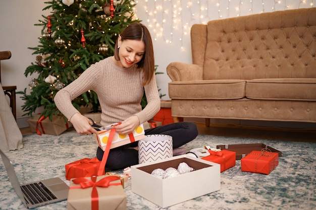 Frau, die Weihnachtsgeschenk verpackt, während sie auf dem Teppich im Wohnzimmer sitzt