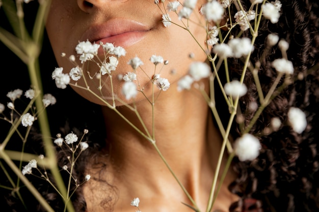 Frau, die weiße Blumen am Gesicht anhält
