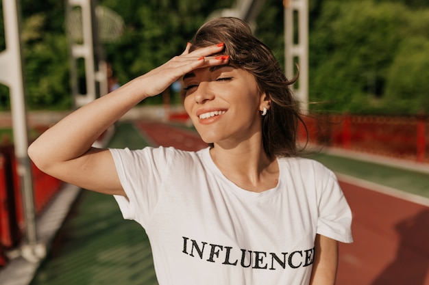 Kostenloses Foto frau, die weißes t-shirt trägt, das auf sonnigem park geht