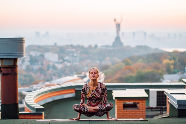 Frau, die Yoga auf dem Dach eines Wolkenkratzers in der Großstadt tut