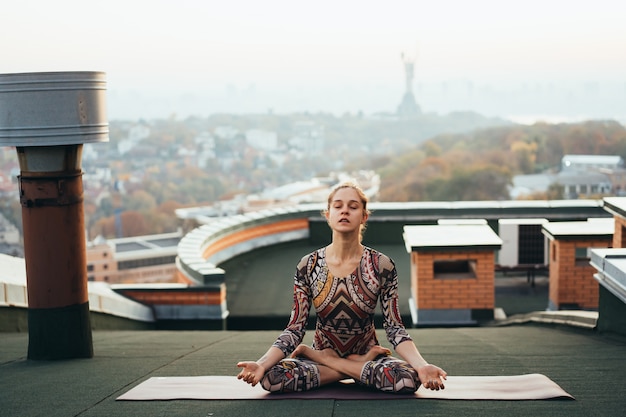 Kostenloses Foto frau, die yoga auf dem dach eines wolkenkratzers in der großstadt tut.