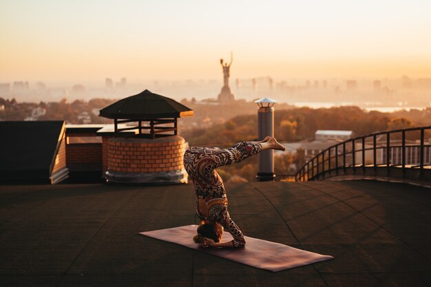 Frau, die Yoga auf dem Dach eines Wolkenkratzers in der Großstadt tut.