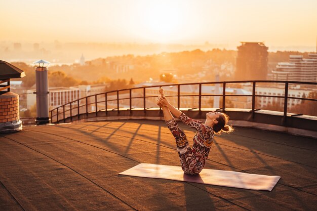 Frau, die Yoga auf dem Dach eines Wolkenkratzers in der Großstadt tut.