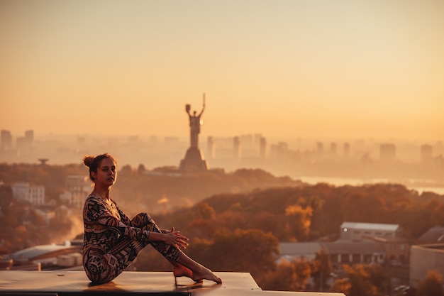 Frau, die Yoga auf dem Dach eines Wolkenkratzers in der Großstadt tut.