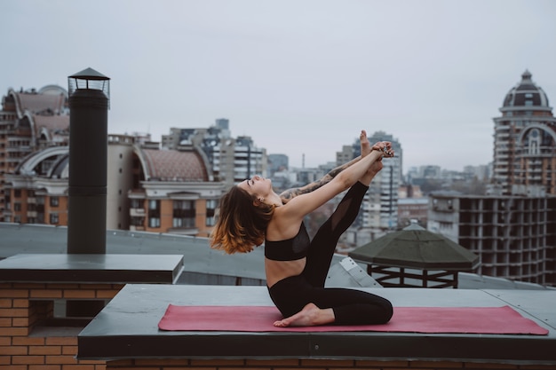 Frau, die Yoga auf der Matte auf dem Dach praktiziert und Yogaübungen macht