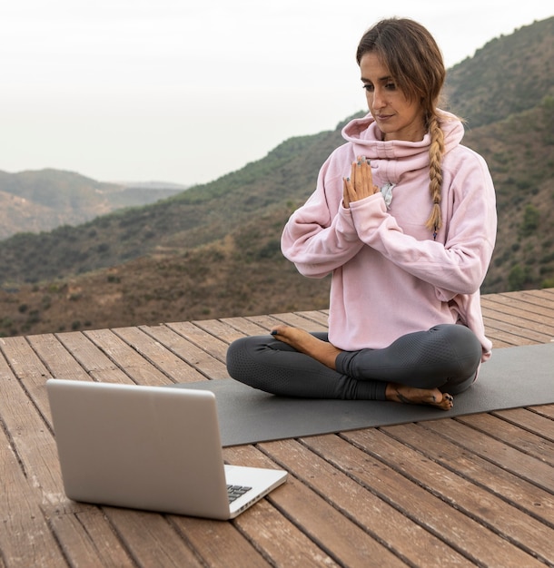 Kostenloses Foto frau, die yoga draußen mit laptop tut