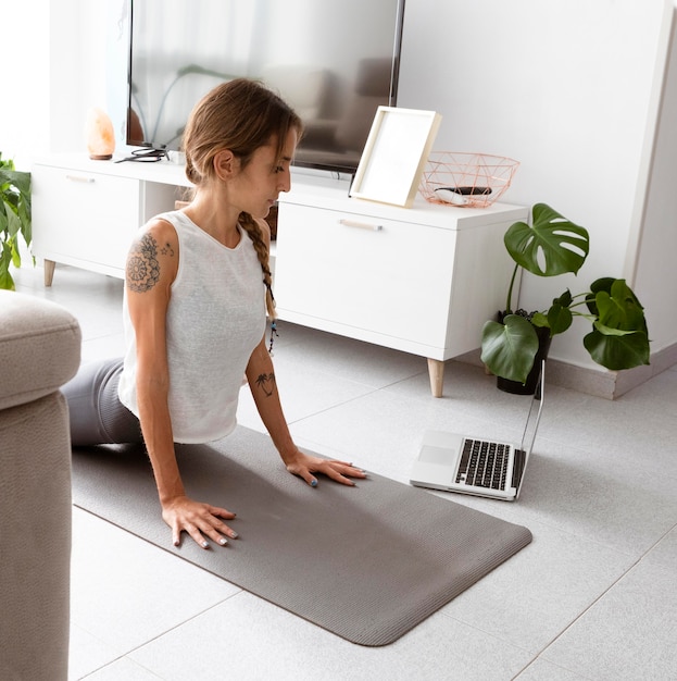 Frau, die Yoga zu Hause auf Matte mit Laptop tut