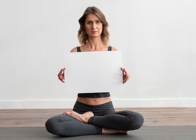 Kostenloses Foto frau, die yoga zu hause tut und leeres plakat hält