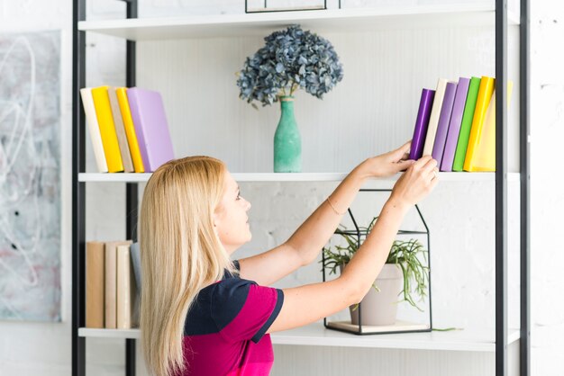 Frau, die zu Hause ein Buch vom Regal wählt