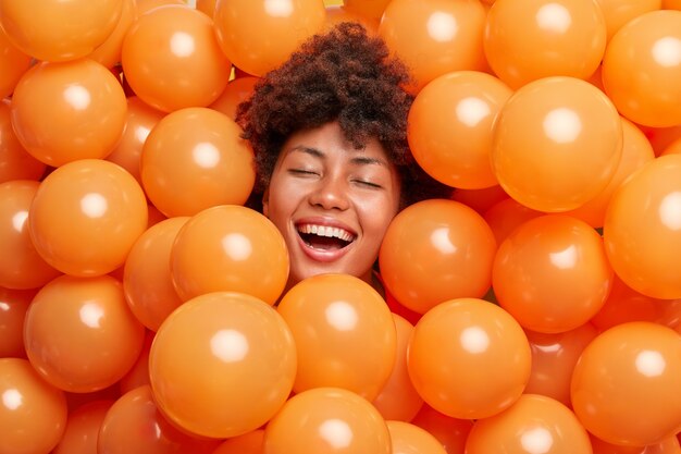 Frau drückt positive Emotionen aus hält die Augen geschlossen lächelt breit von aufgeblasenen Luftballons umgeben