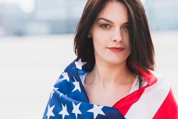 Frau eingewickelt in der amerikanischen Flagge, die patriotisch Kamera betrachtet