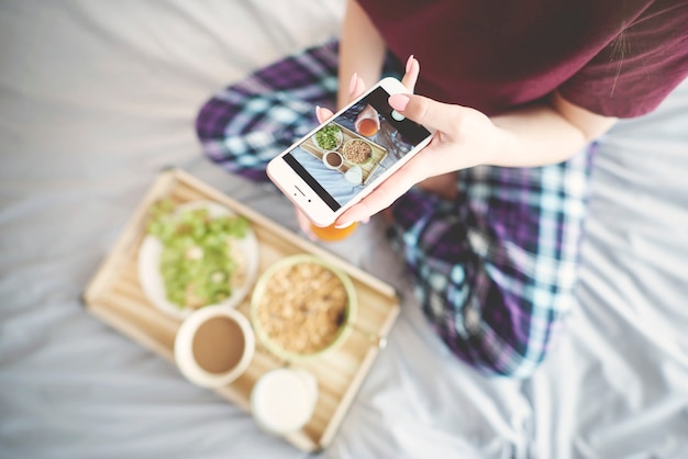 Frau fotografiert Frühstück im Bett