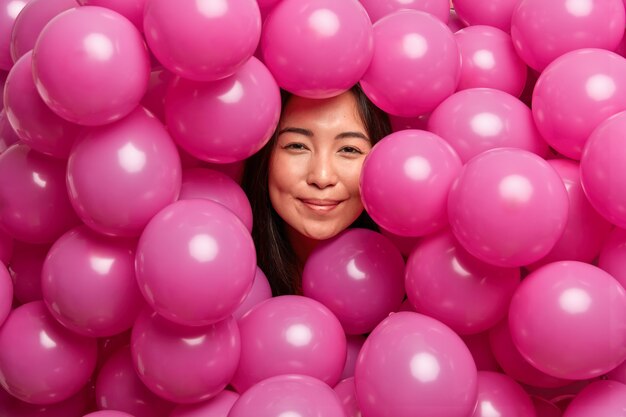 Frau freut sich auf Geburtstagsfeier, umgeben von rosa aufgeblasenen Luftballons