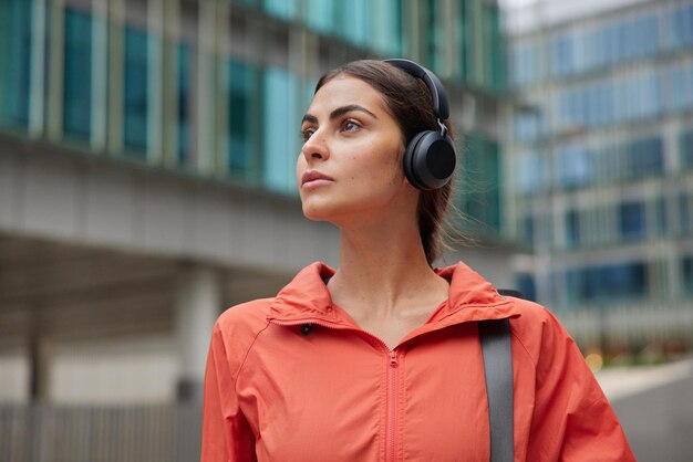 Frau geht im Freien spazieren hört Musik über Kopfhörer trägt Windjacke trägt Karemat-Posen gegen Outdoor