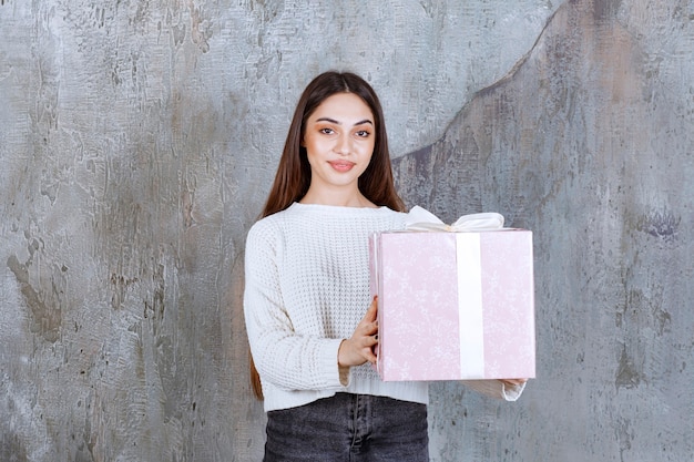 Frau hält eine lila Geschenkbox mit weißem Band umwickelt.