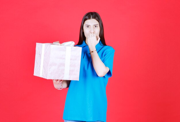 Frau hält eine lila Geschenkbox und sieht verwirrt und nachdenklich aus.