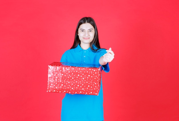 Frau hält eine rote Geschenkbox mit weißen Punkten darauf und bittet um Zahlung.