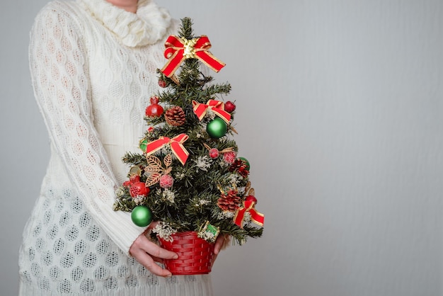 Frau hält einen Weihnachtsbaum auf grauer Wand